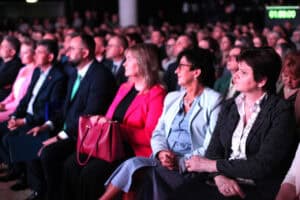 Uczestnicy konferencji siedzą w pierwszym rzędzie widowni. Pierwsza z prawej siedzi Joanna Olszewska.