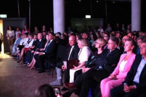Uczestnicy konferencji siedzą w rzędach na ciemnej sali, wśród nich Jarosław Stawiarski.
