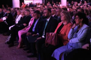 Skupieni uczestnicy konferencji siedzą w pierwszym rzędzie widowni.