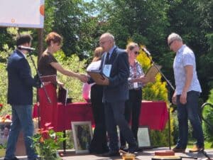 Wręczenie nagrody na scenie – dwie osoby podają sobie ręce i przekazują dyplom podczas jubileuszu PSONI; w tle stoją pozostali uczestnicy uroczystości.