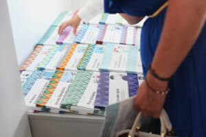 Stół z kolorowymi broszurami edukacyjnymi. Widoczne tytuły publikacji w języku łatwym do czytania, m.in. „Igrzyska Olimpijskie i Paraolimpijskie”, „Moje działania”. Kobieta w niebieskiej sukience sięga po jedną z nich