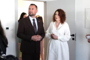 Marek Wojciechowski i Monika Kołtun. Oboje patrzą w tym samym kierunku w bok, mężczyzna ma splecione dłonie. W tle inne osoby.