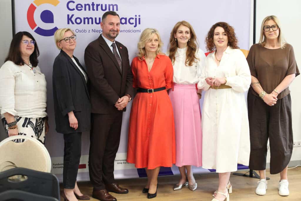 Pamiątkowe zdjęcie grupowe siedmiu osób stojących obok siebie na tle baneru z logo Centrum Komunikacji.