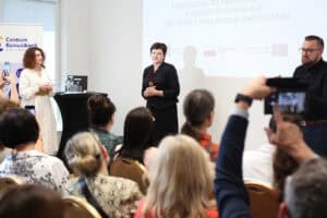 Stoją od lewej: Monika Kołtun, Joanna Olszewska i tłumacz języka migowego; widok z widowni