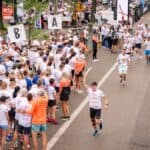 Widok z góry na biegacza wznoszącego pałeczkę sztafetową na trasie biegu, mijającego strefy zmian A i B z dopingującym tłumem.