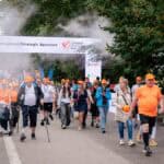 Uczestnicy Poland Business Run 2025, w tym osoby z niepełnosprawnościami i protezami kończyn, przechodzący pod bramą „Sponsorzy Strategiczni” w chmurze wodnej mgiełki.