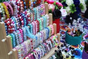 Drewniany stojak z bogatym wyborem ręcznie robionej biżuterii z kolorowych i literowych koralików.