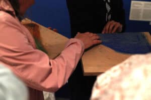 Osoba bada dotykiem drewnianą matrycę drukarską z wyczuwalnymi żłobieniami.