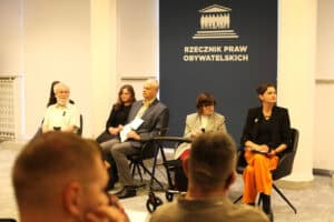 Uczestnicy panelu dyskusyjnego siedzą w rzędzie na tle ściany z logo Biura Rzecznika Praw Obywatelskich.