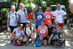 Grupa uczestników w sportowych koszulkach z numerami startowymi pozuje do wspólnego zdjęcia w parku.