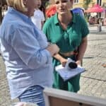 Agnieszka Gruszecka-Sędłak, kierownik Warsztatu Terapii Zajęciowej, udziela wywiadu reporterce Miłce Skalskiej z mikrofonem TVP Info. W tle znajdują się kamienice.