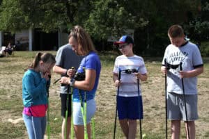 Anna Majerska i grupa młodzieży stoją na trawie z kijkami do Nordic Walking przed rozpoczęciem zajęć