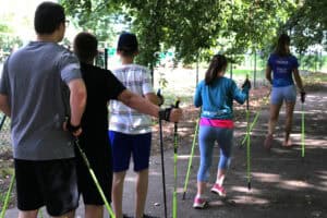 Uczestnicy idą alejką parkową z kijkami do Nordic Walking. Instruktorka prowadzi grupę.