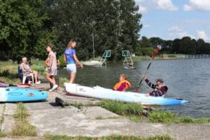 Kobieta i mężczyzna siedzą w kajaku i rozmawiają z instruktorką. Pozostałe uczestniczki siedzą na brzegu.