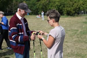 Instruktorka pomaga starszemu mężczyźnie wyregulować kij do Nordic Walking.