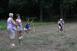 Grupa kobiet na trawniku w parku wykonuje przysiady z kijkami do Nordic Walking.