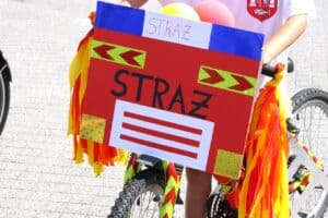 Dziecięcy rower ozdobiony własnoręcznie przygotowaną tablicą z napisem „STRAŻ” i kolorowymi wstążkami.
