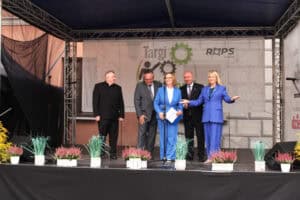 Pięć osób stoi na zadaszonej scenie podczas wydarzenia plenerowego. Od lewej: ks. prałat Tadeusz Pajurek, Zbigniew Wojciechowski, Małgorzata Romanko, Piotr Breś i Anna Augustyniak.