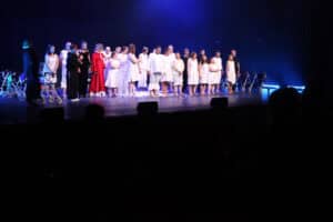 Duża grupa aktorów i twórców stoi w szeregu na scenie i kłania się widowni po występie.