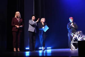 Na scenie teatralnej stoją cztery kobiety, wśród nich Anna Augustyniak, Barbara Danieluk i Maria Pietrusza-Budzyńska. Maria Pietrusza-Budzyńska stoi przy chodziku i trzyma mikrofon.