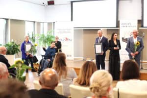 Na scenie stoją nagrodzone osoby, w tym mężczyzna na wózku. Laureaci mają dyplomy i statuetkę. W tle znajdują się banery, w tym „Zostań Lodołamaczem”.