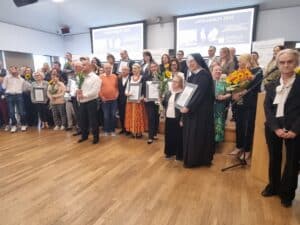 Duża grupa nagrodzonych osób i organizatorów stoi na scenie podczas gali. Trzymają dyplomy i bukiety kwiatów. W tle na ekranach widnieje napis „Lodołamacze 2026”.