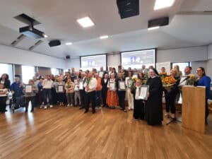 Duża grupa osób stoi na scenie. W pierwszym rzędzie znajduje się zakonnica w habicie, która trzyma certyfikat. W tle na ekranach widnieje napis „Lodołamacze 2026”.