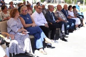 Publiczność siedzi na krzesłach i ogląda występ. W pierwszym rzędzie siedzą kobiety i mężczyźni w eleganckich strojach.