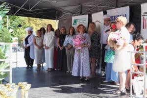Na scenie stoi grupa osób. Po środku Aneta Chęcińska-Baran trzyma duży bukiet kwiatów. Po prawej Agnieszka Niedziałek przemawia do mikrofonu.
