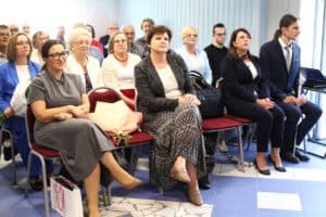 Uczestnicy spotkania siedzą w rzędach czerwonych krzeseł. Wśród nich są Monika Wac i Joanna Olszewska.
