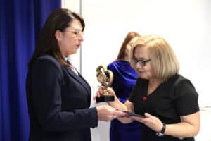 Kobieta w czarnej sukience wręcza Justynie Szafranek pamiątkową statuetkę i dyplom.
