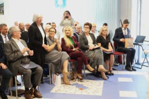 Uczestnicy spotkania siedzą na krzesłach. Po lewej stronie stoi kobieta w czarnym żakiecie. Wśród siedzących są Anna Augustyniak, Joanna Olszewska i Monika Wac.