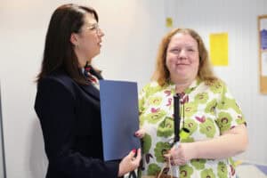 Justyna Szafranek rozmawia z uśmiechniętą Eweliną Orzechowską, która trzyma białą laskę i niebieską teczkę.