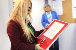 Anna Augustyniak w burgundowym żakiecie ogląda dyplom w czerwonej ramce z medalem.