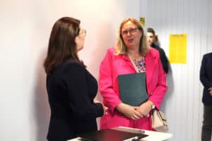Justyna Szafranek stoi tyłem po lewej stronie. Po prawej Justyna Spryszak trzyma ciemną teczkę i patrzy na rozmówczynię.