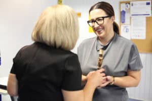 Monika Wac odbiera mosiężną statuetkę od kobiety w czarnej sukience.