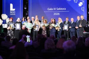 Laureaci i osoby wyróżnione podczas Gali III Sektora 2026 stoją w rzędzie na scenie. Trzymają pamiątkowe dyplomy i bukiety kwiatów.
