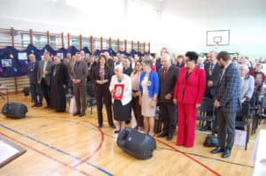 Zaproszeni goście na widowni w sali gimnastycznej. Wśród nich Teresa Irena Jaskulska, prezes Fundacji „Otwórzmy Swoje Serca”, z medalem w dłoniach.