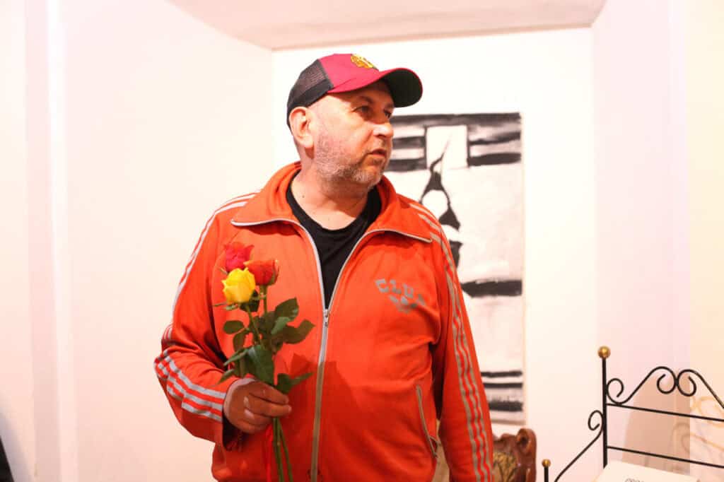 Marcin Wrzal trzyma kilka kolorowych róż. Za nim znajduje się biała ściana z czarno-białym obrazem.