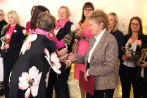 Grażyna Chaberko w sukni w kwiaty wręcza Wandzie Kociubie różę i statuetkę. Wanda Kociuba trzyma czerwoną teczkę.