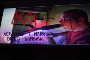 Kadr z filmu: mężczyzna w okularach mówi do mikrofonu. Na ekranie napis „Bigos – Scenariusz i narrator: Daniel Filipowski”.