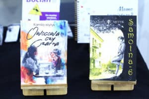Ekspozycja książek Kamili Mytyk pt. „Owocowa czy czarna” oraz „Samotna 6” prezentowana na stojakach na tle innych publikacji autorki.
