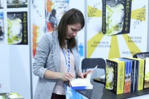 Autorka Kamila Mytyk podpisuje książkę przy stole podczas spotkania autorskiego. Po prawej stronie znajdują się książki autorki.