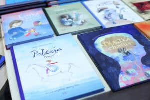 Na stole leżą książki dla dzieci, w tym „Połezja” z ilustracją postaci na białym koniu oraz „Tkaczka chmur”.