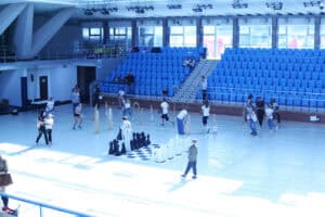Uczestnicy wydarzenia na hali sportowej biorą udział w grach i zabawach sprawnościowych, niektórzy grają na dużej szachownicy, rozłożonej na podłodze.