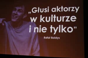 Slajd z tytułem „Głusi aktorzy w kulturze i nie tylko” oraz nazwiskiem Rafał Bołdys. Po lewej stronie znajduje się fragment czarno-białego portretu mężczyzny.