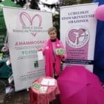 W plenerze stoi stoisko Lubelskiego Stowarzyszenia Amazonek z dwoma roll-upami, różowym stolikiem i amarantową parasolką. Za stolikiem Grażyna Chaberko prezentuje materiały informacyjne.